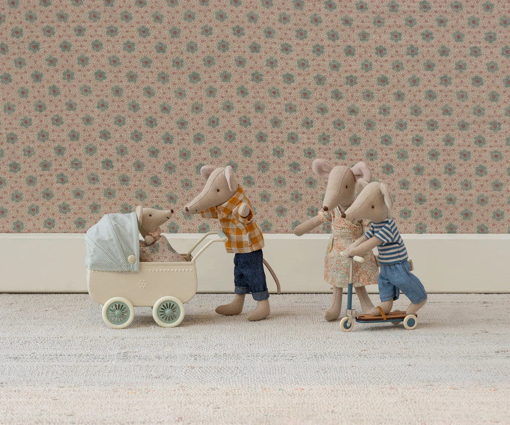 Four Maileg mice stand together: one in a plaid shirt pushes the Maileg Pram With Baby Mouse - Mint, while mice in a dress and stripes ride a scooter. A cozy mouse in a sleeping bag rests nearby, all set against vintage floral wallpaper.