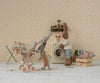 Four plush rabbits are in a vintage laundry room. One pushes two little ones in the Maileg Stroller, Micro - Powder, while another stands by a toy washing machine. Clothes hang on a drying rack nearby.
