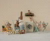 Two stuffed rabbits do laundry in a micro, vintage-style room. One rabbit pushes a Maileg Stroller, Micro - Yellow with a smaller bunny inside, while laundry dries on a rack and a toy washing machine adds to the cozy, whimsical scene.