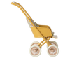 The Maileg Stroller, Micro - Yellow features a vintage-style design with a floral-patterned fabric seat, four white wheels, and a curved handle, displayed in profile against a blurred striped background.