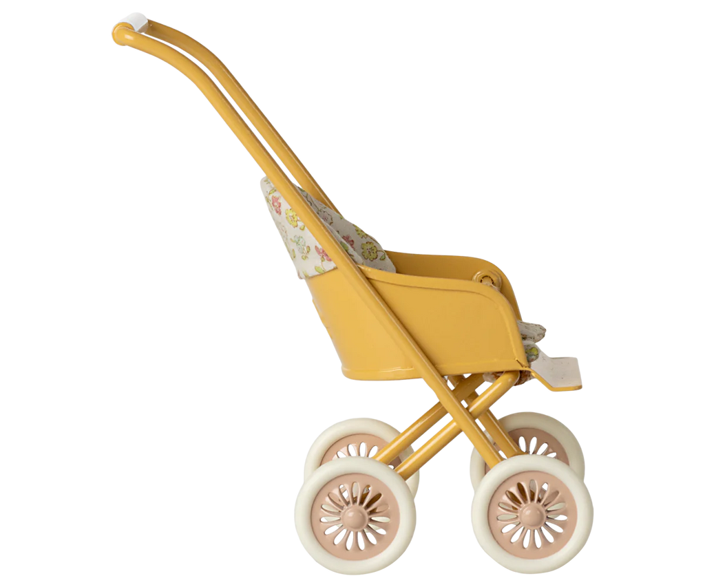 The Maileg Stroller, Micro - Yellow features a vintage-style design with a floral-patterned fabric seat, four white wheels, and a curved handle, displayed in profile against a blurred striped background.