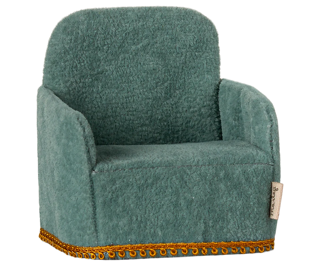 The Maileg Living Room Set includes a small, plush soft chair in green with a high back and armrests, featuring textured fabric and gold trim along the bottom edge—ideal for cozy evenings by a Maileg Fireplace.