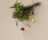 A decorative wall arrangement of twigs and greenery features metal ornaments with handpainted details, including the Maileg Metal Ornament Trumpet in Dark Green. This charming piece, along with red and white mushrooms, a drum, and a gold star, brings a festive spirit reminiscent of Christmas tree decorations.