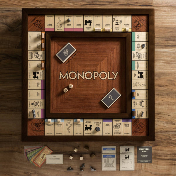 The Monopoly Heirloom Edition is a customized wooden board with engraved property spaces, cards, dice, money, tokens, and pieces on a walnut cabinet surface. The center is proudly inscribed with "MONOPOLY." Perfect for Monopoly enthusiasts.