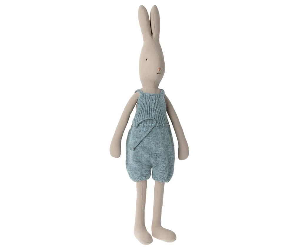 The Maileg Rabbit size 4 from the Bunny & Rabbit collection wears a knitted blue romper. Made of natural linen, it features a simple design with long ears, a soft beige color, and arms hanging by its sides while standing against a plain white background.