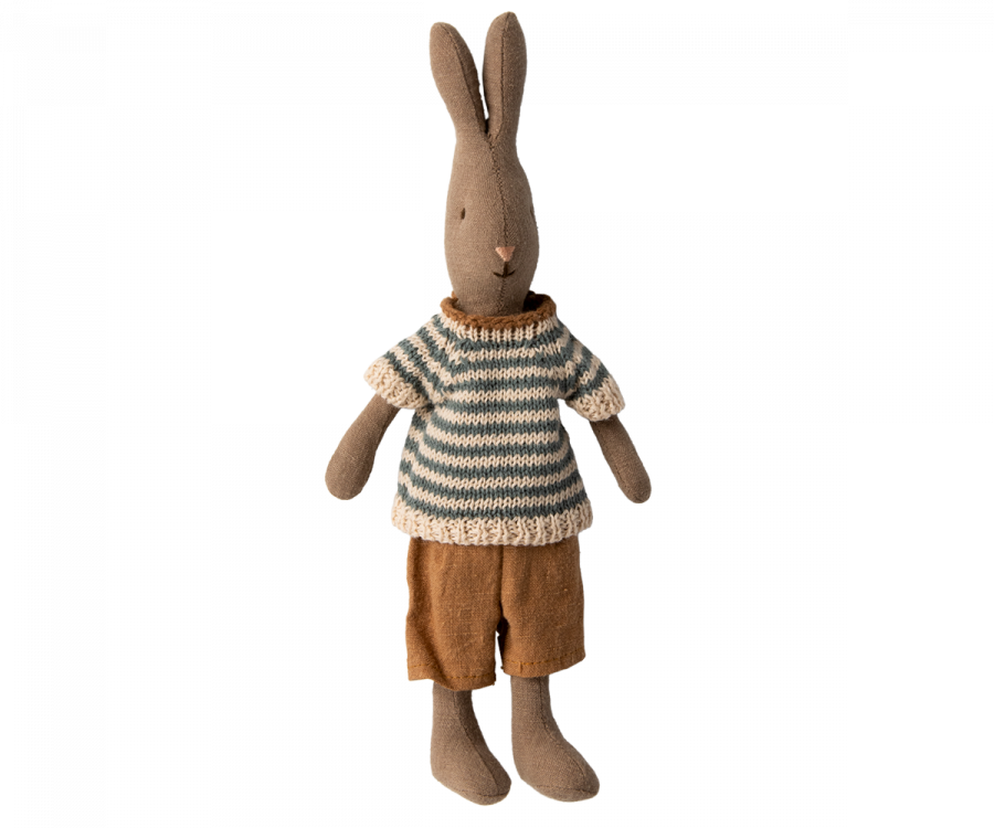 A soft natural linen rabbit with long ears stands upright. It is dressed in a knitted, blue and white striped sweater and brown pants. The bunny's wardrobe boasts a simple, minimalist design with a neutral expression, making it a charming addition to any Maileg Rabbit Size 1 - Brown - Shirt And Shorts dollhouse.