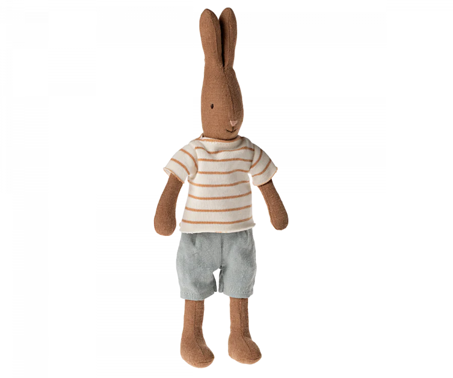 The Easter Basket Set features a plush rabbit doll, sporting a white and brown striped shirt and light blue shorts. Standing upright with long ears and a simple stitched face, it captures the charm of handmade Bolgatanga baskets.