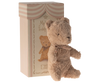 The Maileg My First Teddy, Powder, a small plush bear with a vintage look and brown ribbon, sits beside a striped cardboard box. This perfect newborn gift features an illustration of the teddy bear and decorative text.