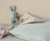 The Maileg Bunny Rattle Set - Mint rests on pastel floral bedding, complemented by wallpaper with delicate blue flowers. Made from soft cotton in pink and blue tones, the bedding creates a cozy and serene ambiance.