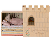 A Maileg Fairytale Set features a toy mouse dressed as a princess on colorful mattresses in a box resembling the Maileg Castle Hall, showcasing "The Princess and the Pea" title with a heart-shaped window.