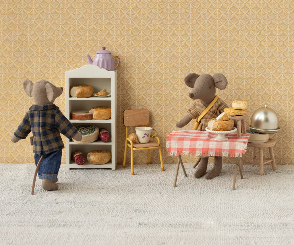 In a tiny kitchen, Maileg Mum Mouse, light brown in a plaid shirt and jeans, is by the bread shelf with mouse furniture. Across the room, another mouse in a cotton scarf sits at a red-checkered table with pies and a cloche. A teapot rests on the shelf. (Ships in one week.).