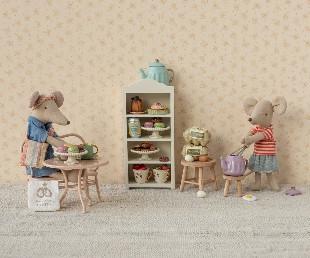 Two mice, dressed in charming outfits, sit at a tiny table with teacups. Nearby are pastries on a shelf, stools, and an egg frying. One mouse sports a sun hat and apron; the other dons a striped shirt with the product "Maileg Denim Dress And Bag For Mum Mouse.