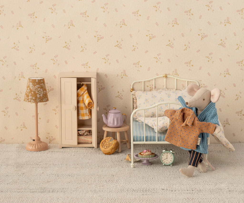 A cozy miniature scene includes a small metal bed with polka dot bedding, a cupboard with mouse clothes, a teapot, pastries, an alarm clock on the floor, and an elephant plush toy wearing Maileg's shirt and striped pants for Dad Mouse. Nearby stands a floral lamp.
