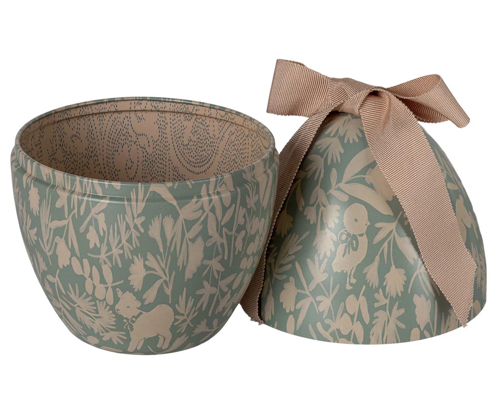 The Easter Basket Set is an egg-shaped container with a green floral and animal pattern, divided into two halves. The top features a beige bow, and the interior echoes the intricate design of hand-made elephant grass baskets.