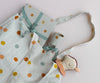 The Maileg Tote Bag With Multi Dots - Small, in light gray linen with colorful polka dots, includes a matching rolled-up cloth and a soft toy featuring a pink checkered scarf. Another fabric item is elegantly wrapped with a ribbon, all presented in a minimalist pastel color scheme.