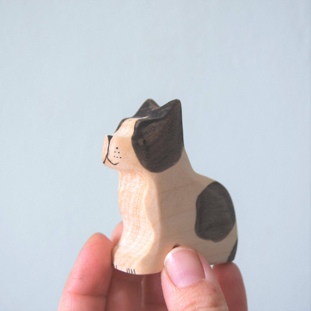 A hand cradles a small, intricately crafted wooden French Bulldog figurine, painted in black and white. Made from sustainable hardwood, this charming piece sits upright against a plain light gray background.