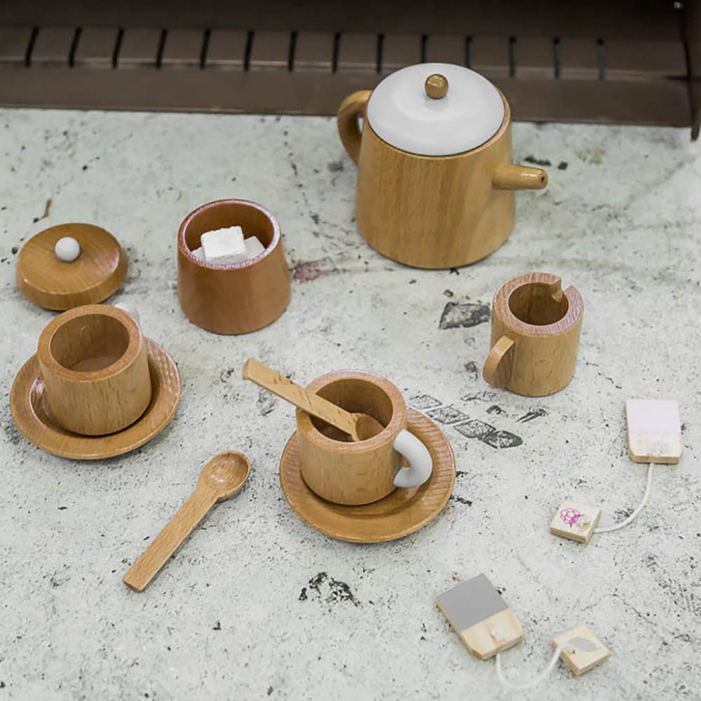 The Wooden Tea Set, comprised of a teapot, cups, kettle, lid, spoon, and two tea bags on a textured surface, is ideal for creative chai latte play.