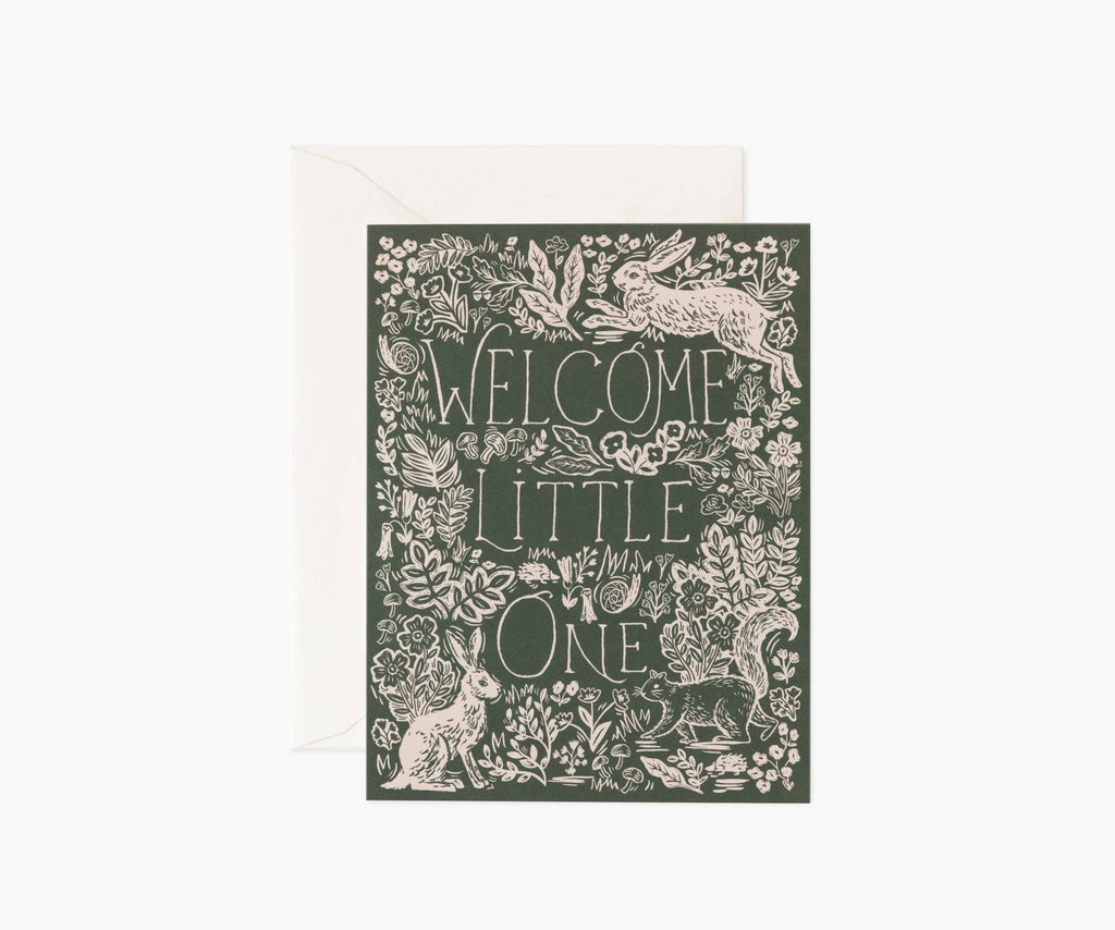 The Fable Baby Card features a dark green cover with “Welcome Little One” in bold letters, surrounded by white flowers, leaves, and rabbits. It has a blank interior for your message and comes with a white envelope.