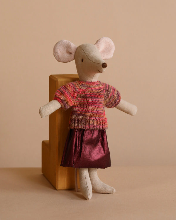 Against a wooden block, the Maileg Mom Mouse With Extra Outfit - Petite Couture wears a colorful knitted blouse and shiny pink skirt. The neutral background complements her attire's soft hues.