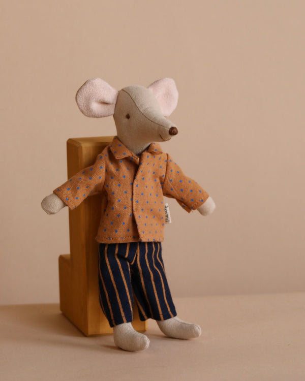 The Maileg Dad Mouse with Extra Outfit sits against a wooden block, adorned in a brown jacket with blue spots and dark striped pants, making its adorable outfit stand out against the neutral beige background.