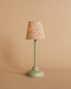 The Maileg Little Sister Bedtime Set features a small vintage-style table lamp with a pale green base and a lampshade adorned with red and light blue floral patterns, ideal for complementing Mouse Furniture or accenting a Maileg Vintage Bed.