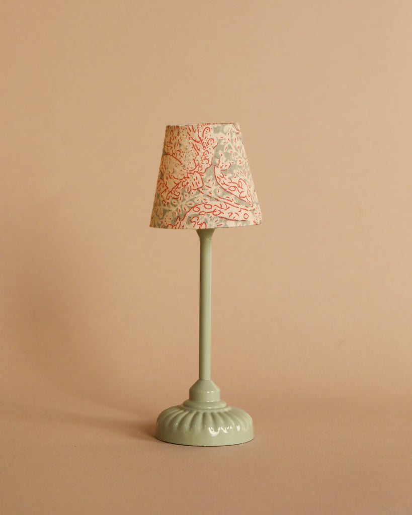 The Maileg Little Sister Bedtime Set features a small vintage-style table lamp with a pale green base and a lampshade adorned with red and light blue floral patterns, ideal for complementing Mouse Furniture or accenting a Maileg Vintage Bed.