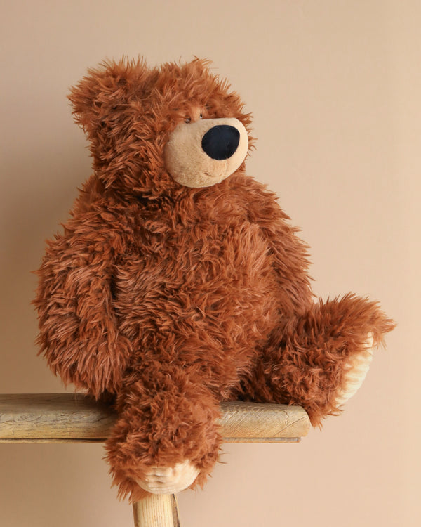 A Brown Bear Weighted Stuffed Animal 15" with a dark nose sits on a wooden stool against a beige background, looking slightly to the right, inviting warm hugs and cozy moments.