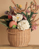 The Basket Of Felt Flowers is a woven basket filled with eco-friendly felt blooms, including daisies and roses. These vibrant, handcrafted flowers are artfully arranged in an organic style against a neutral background.