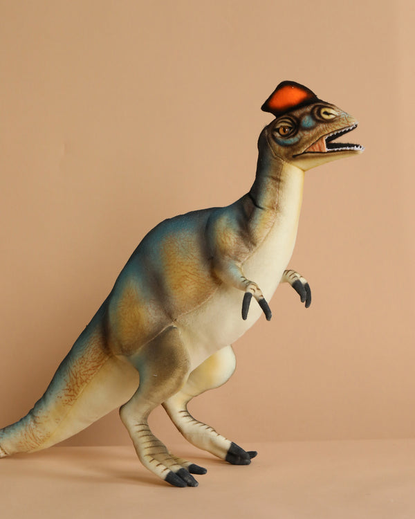 The Dilophosaurus Dinosaur Stuffed Animal features a hand-sewn design with a red crest. It stands on two legs, against a beige background, showcasing a blue and beige body with an open mouth and short arms for added character.