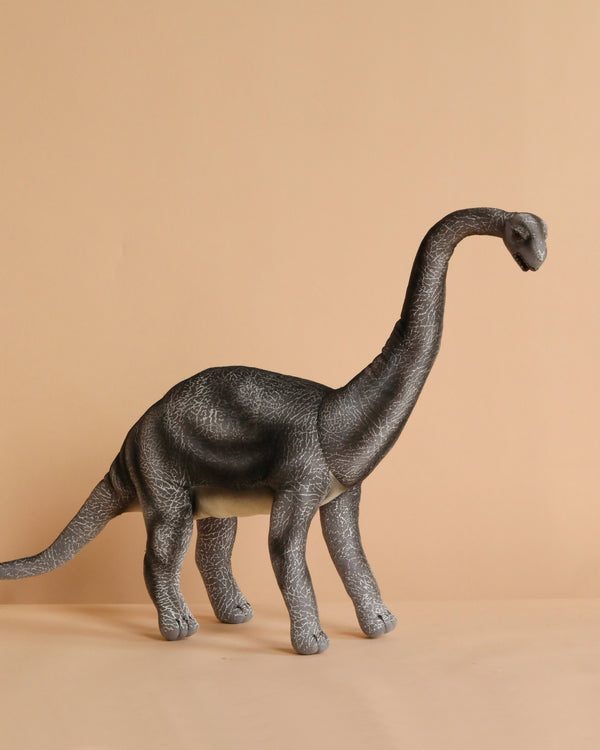 A gray Diamantinasaurus Dinosaur Stuffed Animal stands on a neutral beige background, featuring realistic details such as a long neck, small head, and thick tail.
