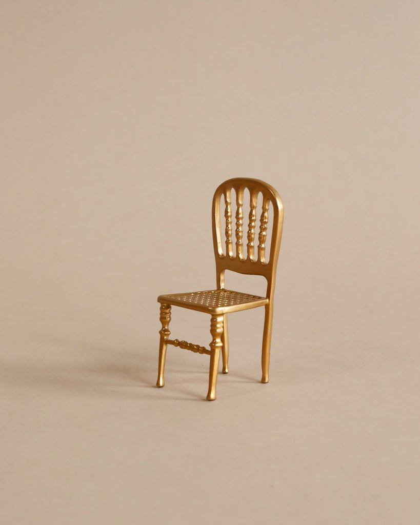 A small, elegant gold chair with vertical slats and a patterned seat sits gracefully beside a Maileg Kitchen Set on a light neutral background.