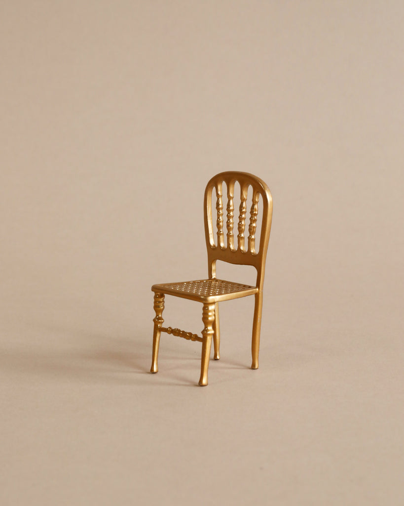 A small, ornate chair from the Maileg Dining Room Set, featuring a spindle back and detailed legs, is set against a plain beige background, adding elegance to any setting.