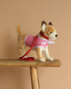 A Chihuahua with Coat & Leash stuffed animal, featuring realistic hand-sewn details, stands on a wooden bench against a beige background wearing a pink harness and red leash.
