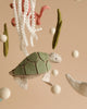 A close-up of a whimsical felt mobile, **Handmade Mobile - On The Reef - Final Sale**, featuring a green sea turtle with a patchwork shell, white fluffy balls, and seaweed-like felt pieces hanging from strings. Perfect for nursery decoration and visual development, the soft beige background adds to the overall gentle and soothing feel.