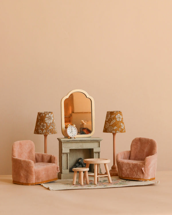 The Maileg Living Room Set features a vintage-style arrangement with two pink velvet armchairs, a small table, floral lamps, a fireplace with a clock and mirror, and a tiny bird figurine on a soft beige background.