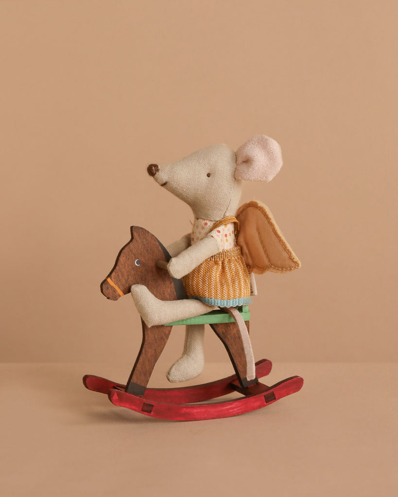 The Maileg Little Sister on Rocking Horse Set features a small mouse in fairy clothes with wings and a dress, seated atop a wooden rocking horse against a plain beige background.