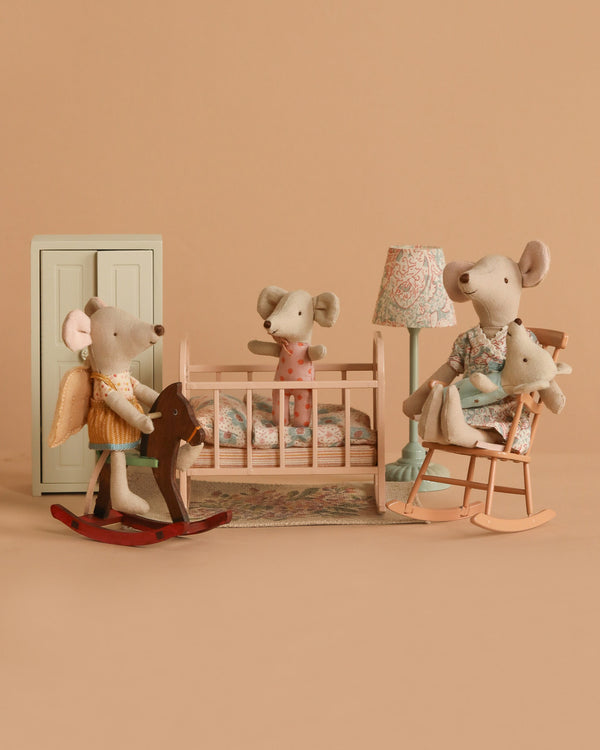 The Maileg Nursery Set With Mice features four mice—one in a crib, one on a rocking horse, and two in a rocking chair—amid pastel furniture and muted tones.