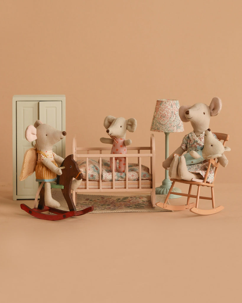 The Maileg Nursery Set With Mice features four mice—one in a crib, one on a rocking horse, and two in a rocking chair—amid pastel furniture and muted tones.