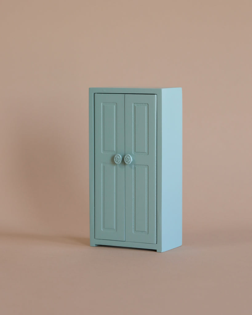 A small, light blue cabinet with double doors and round handles stands against a plain beige background, perfect for storing the Maileg Little Sister Bedtime Set or pairing with other Mouse Furniture.