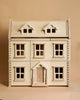 The PlanToys Victorian Dollhouse is a sustainably crafted wooden dollhouse with a natural finish, featuring a symmetrical facade and a triangular roof. It includes six framed windows and a centered door, all set against a plain beige background.