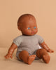 The Minikane Soft Body Doll (11”) - Suzie features curly textured hair, blue eyes, an open mouth, and a light gray romper. Crafted from phthalate-free vinyl, Suzie inspires imaginative play as she sits upright on a beige background.
