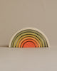 A set of colorful wooden nesting arches forming a rainbow, arranged from largest to smallest with non-toxic paint in muted colors including green, yellow, and orange, against a plain beige background.