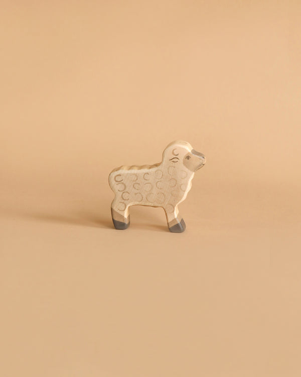 A wooden toy sheep with a light tan body, grey hooves, and subtle circular patterns is standing on a beige background. Handcrafted in Europe, this Holztiger Lamb boasts a simple and minimalist design.