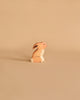 A small, handcrafted wooden rabbit figurine with a minimalist design stands on a beige surface. Part of the "Noah's Ark With Animals" set, it's crafted from solid wood in Holztiger style. The light brown rabbit features white accents against its matching beige background.