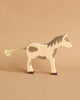 A Holztiger wooden horse figure from Noah's Ark with Animals features a simple design and brown patches on a beige surface, its braided tail adding charm. The matching background enhances the natural tones of this solid wood toy.