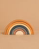 The Handmade Rainbow Stacker - Mustard features five wooden arches in muted earth tones, crafted with non-toxic paint for safe play. Arches stack from largest to smallest and are pictured on a beige background.