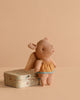 The Maileg Pig In A Box With Fairy Outfit, dressed in yellow and blue fairy clothes, stands beside a playful tin on a beige background—an adorable gift for any baby girl.
