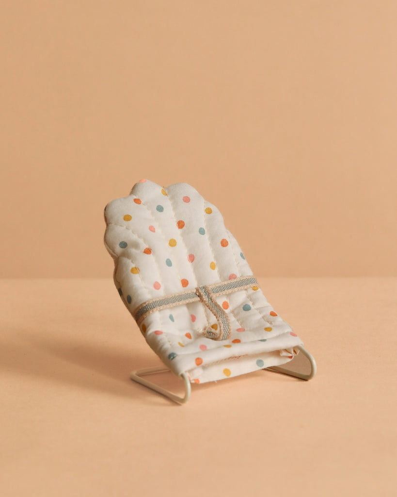 The Maileg Sleepy Wakey Baby Mouse In Bouncer features a small, polka-dotted fabric chair with a thin metal frame, perfect for your mouse to relax in soft fabrics—a charming miniature accessory for imaginative play.