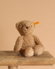 The Thommy Teddy Bear Brown Plush Toy, 8 inches, with a yellow "Steiff" ear tag, sits on a wooden surface against a beige background.