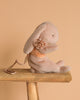 A soft, light pink Maileg Plush Sleeping Bunny With Harness sits on a wooden bench against a beige background.